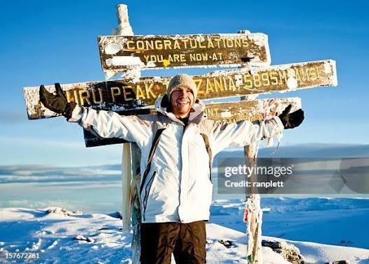 Trekkers celebrating at Uhuru Peak summit sign on Mount Kilimanjaro via Umbwe Route